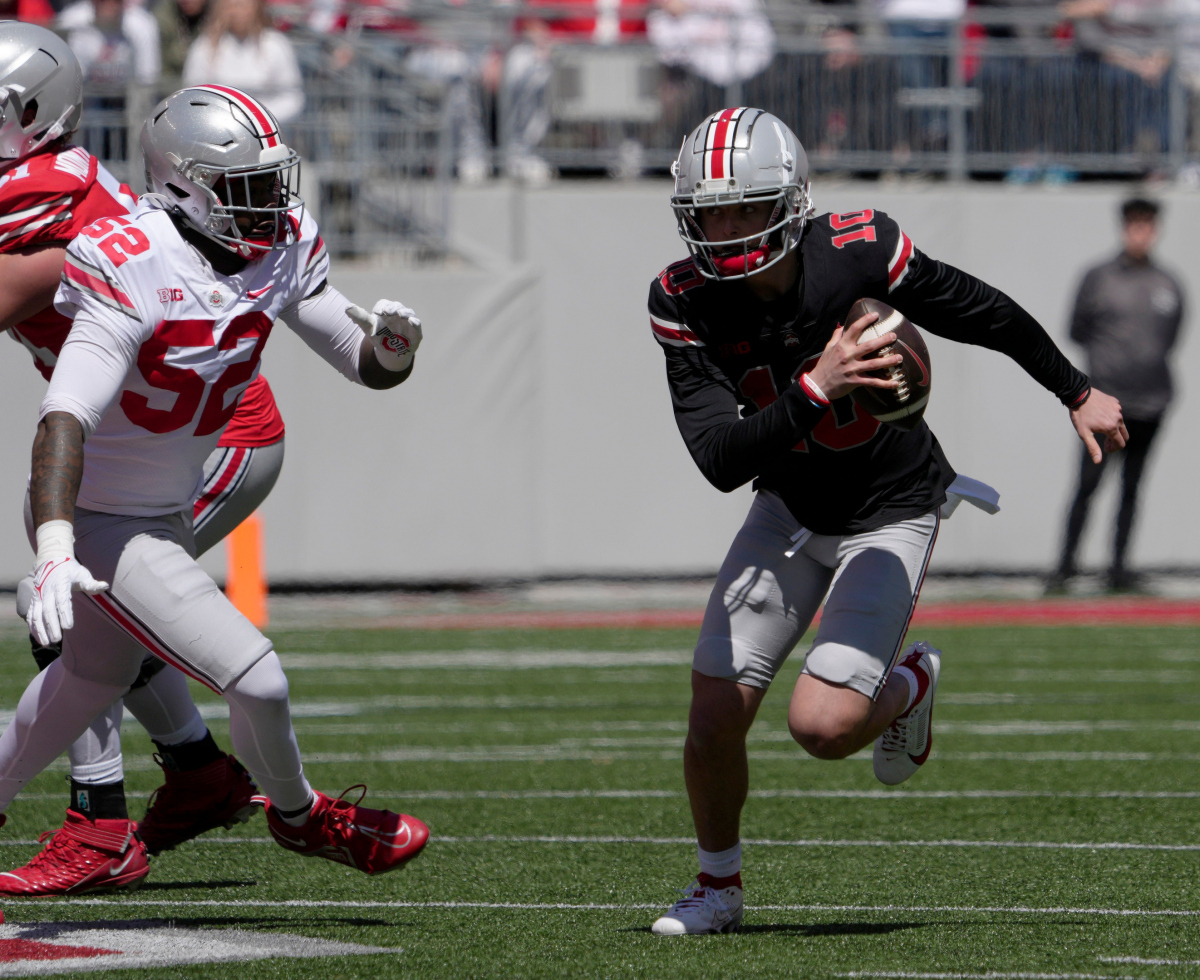 Julian Sayin (10) runs the football for the scarlet team while pursued by defensive end Josh Mickens (52) of the gray team during the first half of the LifeSports spring football game at Ohio Stadium on Saturday.